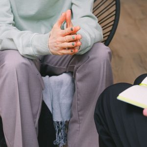 Crop unrecognizable psychotherapist taking notes in journal while interacting with woman on chair during psychological counseling indoors
